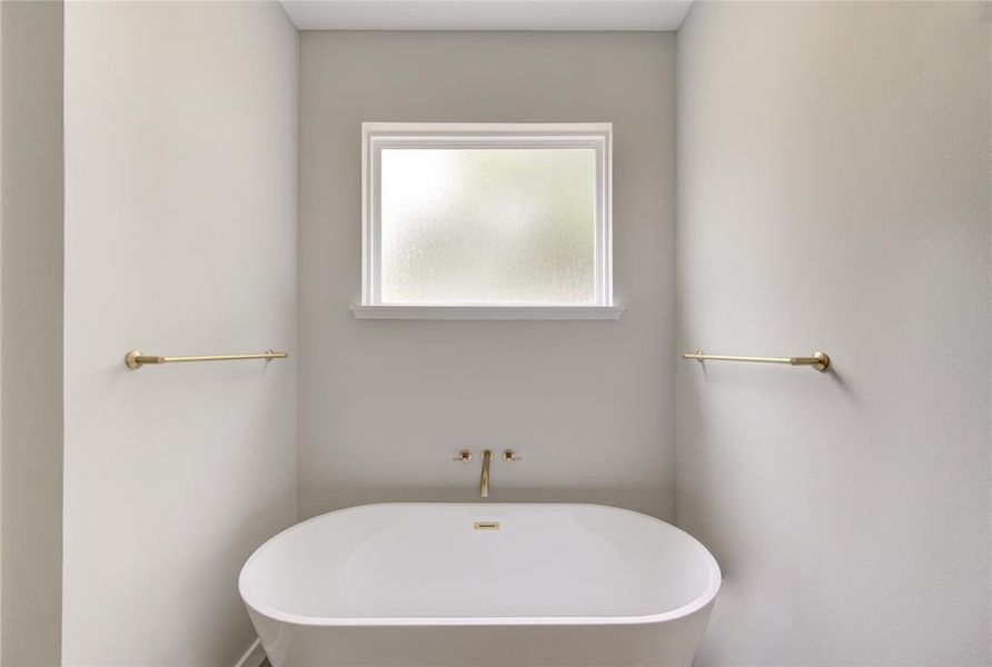 Large soaking tub under large opaque window allows for privacy and natural light