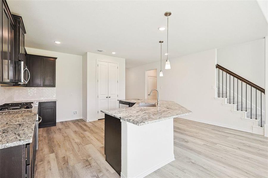 Kitchen featuring light hardwood / wood-style floors, sink, backsplash, and a center island with sink