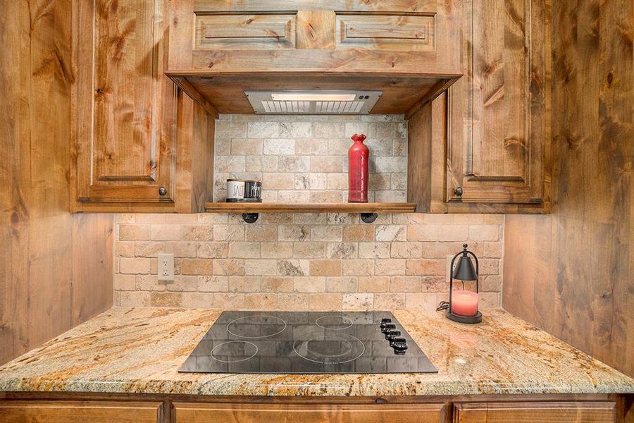 Kitchen with black electric cooktop, light stone countertops, and backsplash