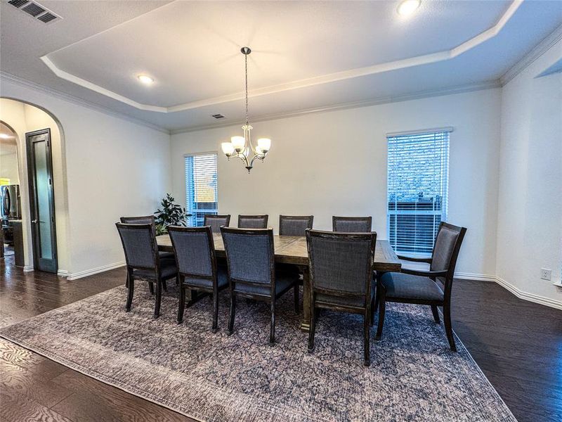 Dining room with crown molding, a notable chandelier, a raised ceiling, and dark hardwood / wood-style flooring