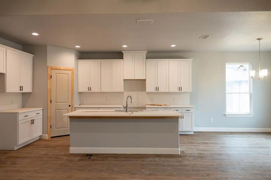 Kitchen featuring white cabinetry, wood-type flooring, and a center island with sink