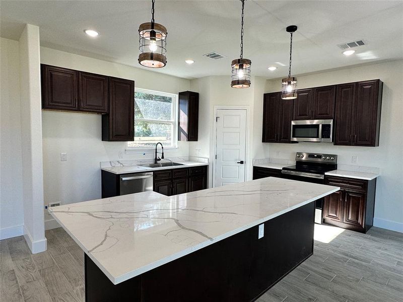 Kitchen featuring sink, light wood-type flooring, appliances with stainless steel finishes, a kitchen island, and pendant lighting