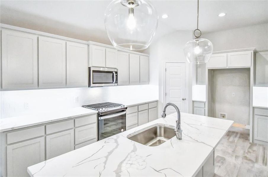 Kitchen with appliances with stainless steel finishes, hanging light fixtures, light stone countertops, and sink