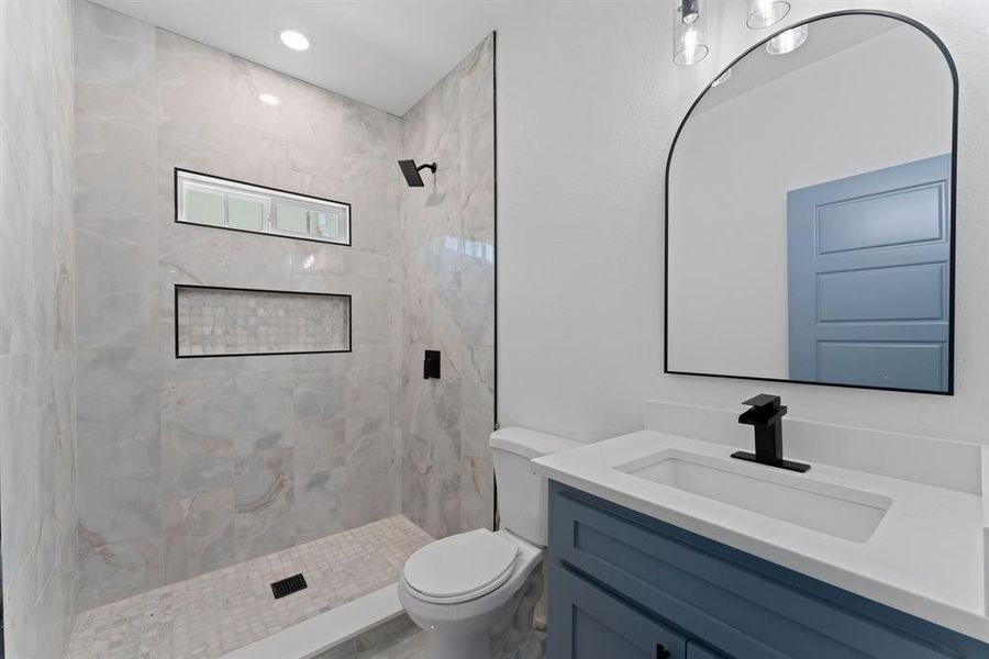 Bathroom featuring a tile shower, vanity, and toilet