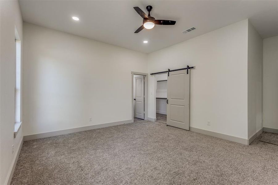 Unfurnished bedroom featuring carpet, a barn door, ceiling fan, and a closet