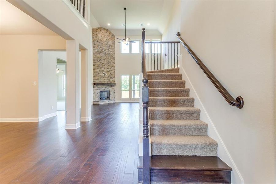 Stairs featuring ceiling fan, hardwood / wood-style floors, a stone fireplace, and a high ceiling