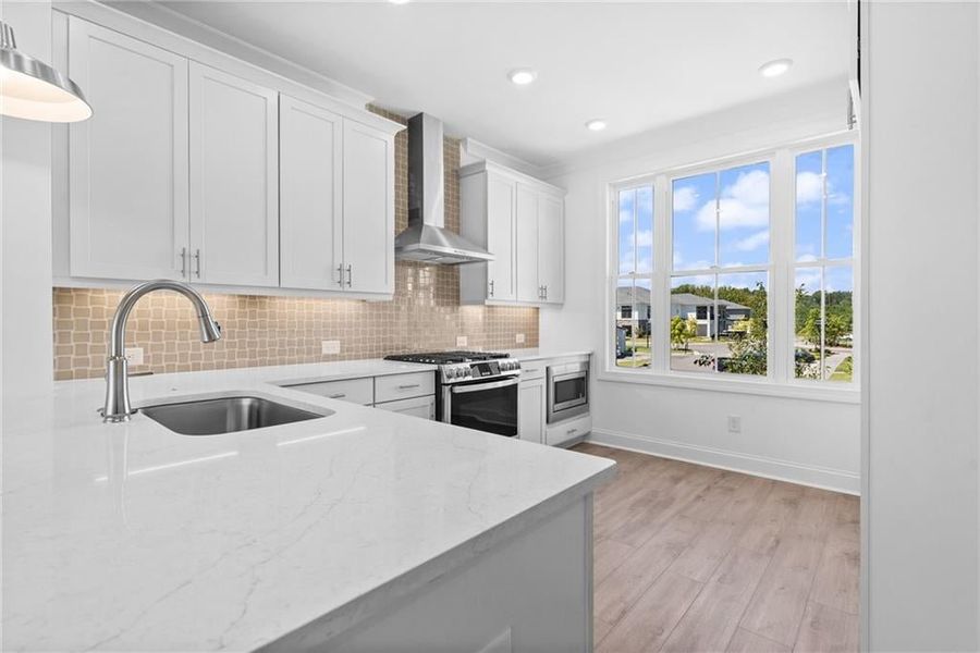 Kitchen featuring stainless steel appliances, white cabinets, sink, hard surface floors, and wall chimney range hood