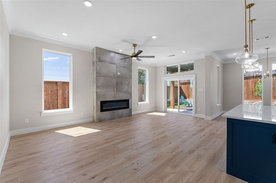 Unfurnished living room with light wood-type flooring, ceiling fan with notable chandelier, a fireplace, and crown molding