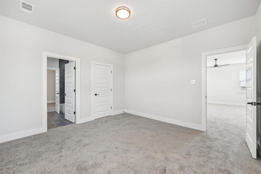 Unfurnished bedroom with ensuite bathroom, dark colored carpet, and a closet