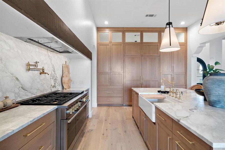 Kitchen with high end stainless steel range oven, light stone counters, backsplash, decorative light fixtures, and light wood-type flooring