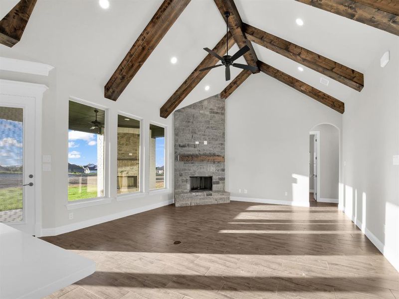 Unfurnished living room featuring hardwood / wood-style flooring, ceiling fan, a stone fireplace, high vaulted ceiling, and beamed ceiling