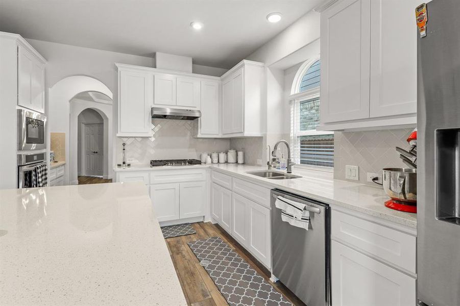 Kitchen with light stone counters, sink, white cabinets, stainless steel appliances, and dark hardwood / wood-style flooring