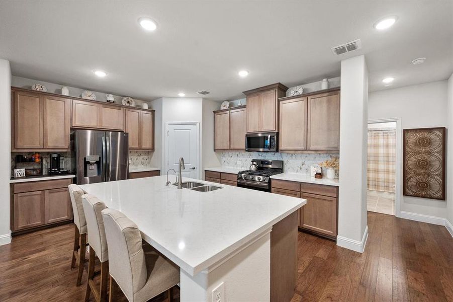 Kitchen with dark hardwood / wood-style floors, stainless steel appliances, sink, and a center island with sink