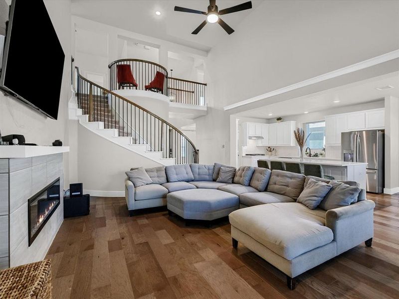 Living room with a high ceiling, a tiled fireplace, sink, hardwood / wood-style floors, and ceiling fan