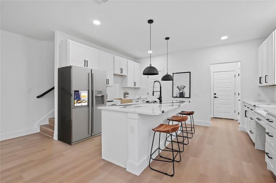 Kitchen featuring a large island, white cabinetry, light hardwood / wood-style floors, and stainless steel fridge with ice dispenser