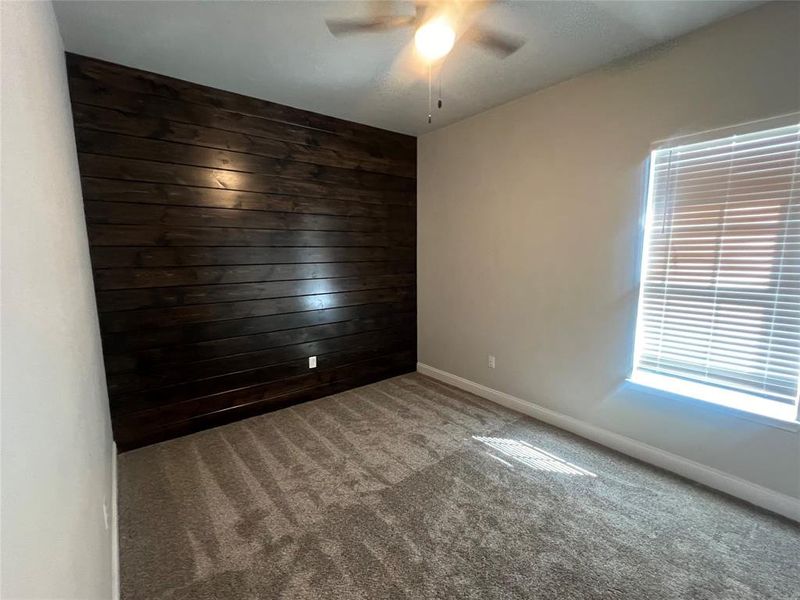 Spare room featuring carpet, wooden walls, and ceiling fan