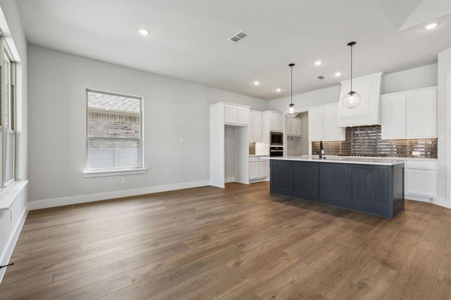 Kitchen featuring a center island with sink, hardwood / wood-style flooring, decorative light fixtures, and white cabinets