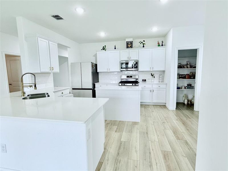 Kitchen with sink, appliances with stainless steel finishes, backsplash, light hardwood / wood-style flooring, and white cabinets