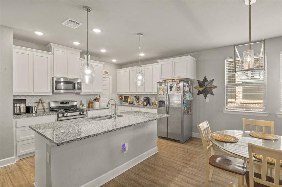 Kitchen with appliances with stainless steel finishes, sink, backsplash, light wood-type flooring, and white cabinetry