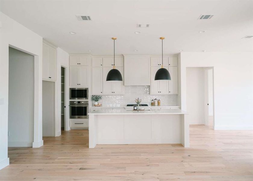 Kitchen with stainless steel appliances, light hardwood / wood-style floors, white cabinets, and a kitchen island with sink