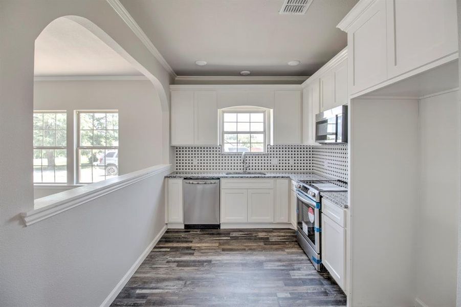 Kitchen featuring dark hardwood / wood-style flooring, tasteful backsplash, crown molding, appliances with stainless steel finishes, and sink