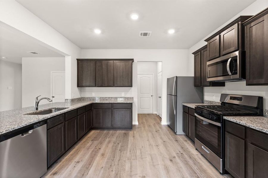 Kitchen featuring stainless steel appliances, sink, light stone countertops, and light hardwood / wood-style floors