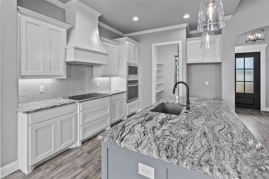 Kitchen with white cabinets, custom exhaust hood, appliances with stainless steel finishes, decorative backsplash, and sink