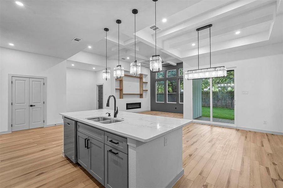 Kitchen featuring a center island with sink, light hardwood / wood-style flooring, pendant lighting, dishwasher, and sink