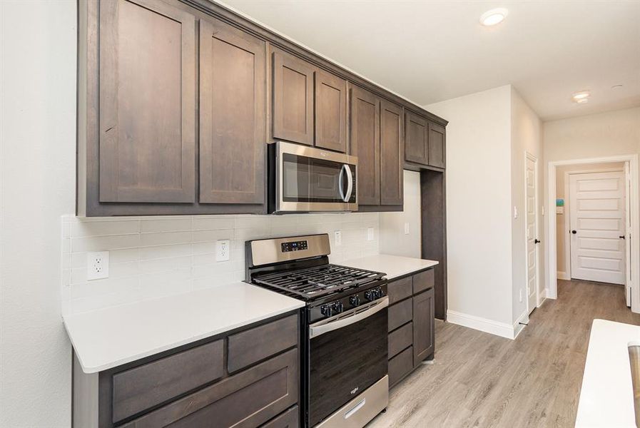 Kitchen featuring appliances with stainless steel finishes, dark brown cabinets, light wood-type flooring, and backsplash