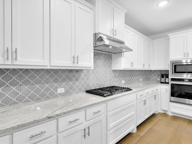 Kitchen with white cabinetry, stainless steel appliances, light hardwood / wood-style flooring, and tasteful backsplash