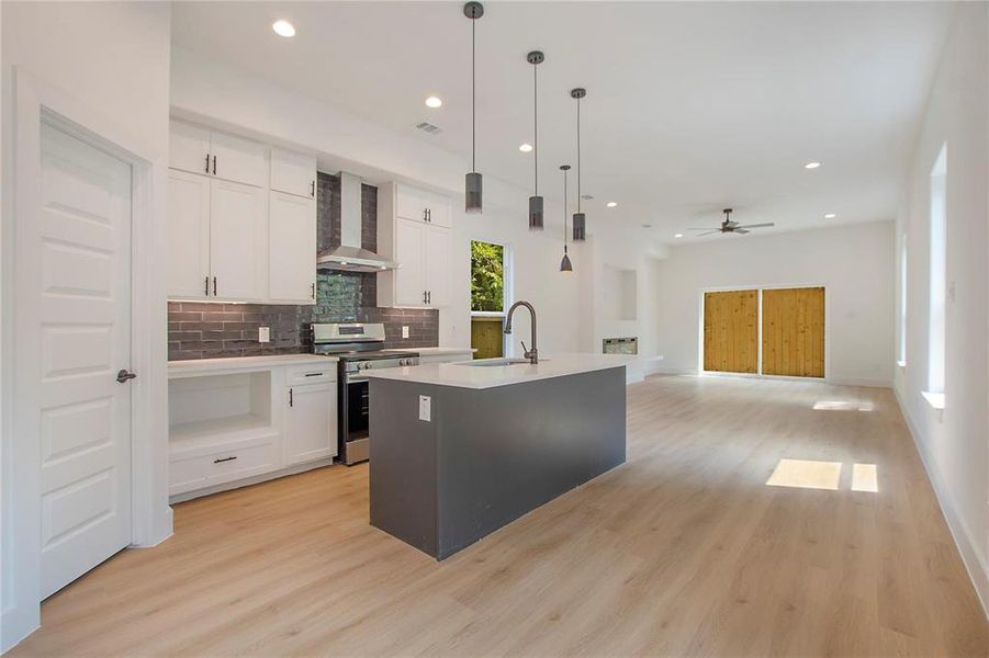 Kitchen featuring wall chimney range hood, a kitchen island with sink, pendant lighting, stainless steel range oven, and white cabinets