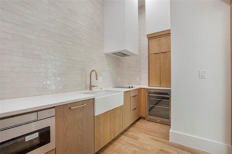 Hidden Prep kitchen #2 featuring wine cooler, sink, decorative backsplash, light wood-type flooring, and cooktop