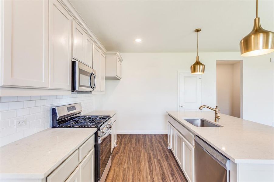 Kitchen featuring hanging light fixtures, sink, appliances with stainless steel finishes, backsplash, and dark wood-type flooring