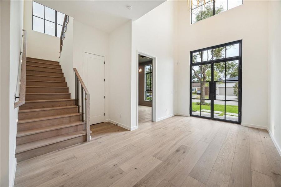 Enter through a bright and open foyer featuring a modern staircase with wood steps and sleek iron railings. The large windows and glass front door bring in natural light, creating a welcoming first impression.