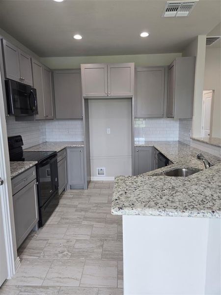 Kitchen with light stone countertops, tasteful backsplash, stove, and kitchen peninsula