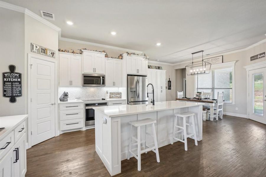 Kitchen with a kitchen island with sink, stainless steel appliances, dark hardwood / wood-style flooring, and white cabinetry