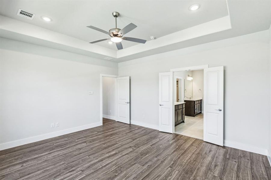 Unfurnished bedroom with a tray ceiling, ensuite bathroom, ceiling fan, and light hardwood / wood-style floors