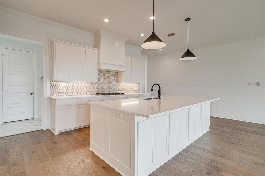 Kitchen with an island with sink, sink, light wood-type flooring, and white cabinetry