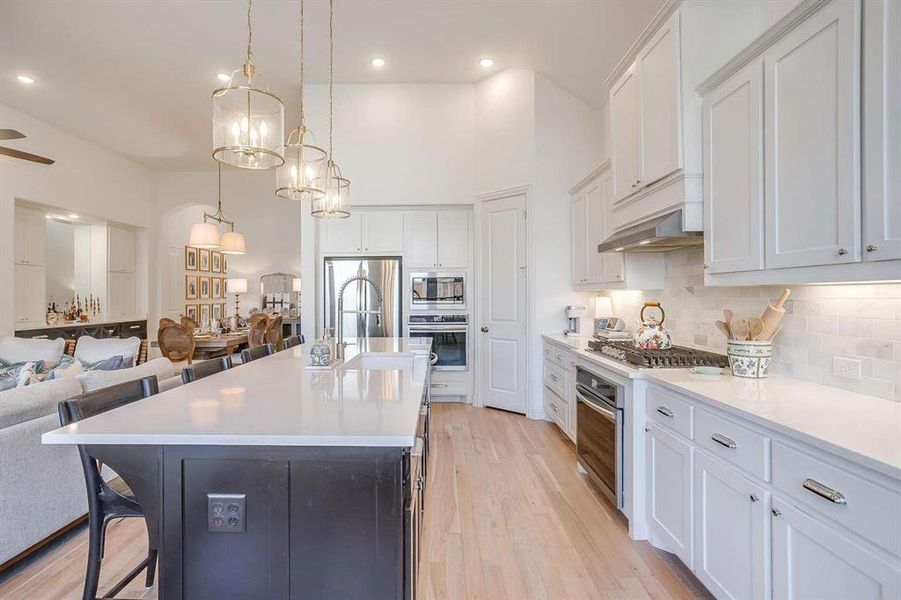 Kitchen with sink, stainless steel appliances, a center island with sink, white cabinets, and light wood-type flooring