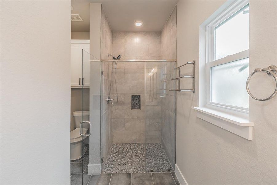Primary Bathroom featuring walk in shower, tile flooring, and toilet