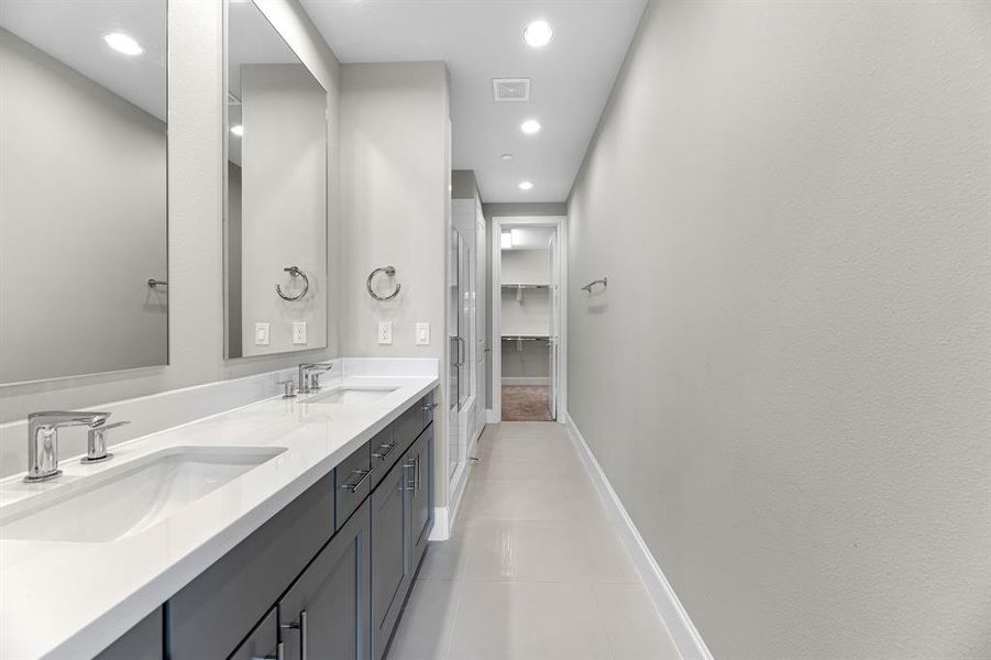 The luxurious ensuite bathroom features sleek finishes that create a modern and sophisticated look. Stunning contrasting quartz countertops beautifully complement the gray-toned cabinets, adding both elegance and functionality to the space.