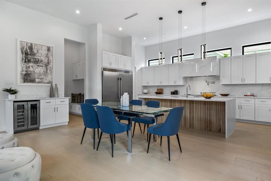 Dining area with light hardwood / wood-style flooring, beverage cooler, sink, and a towering ceiling