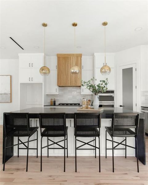 Kitchen featuring white cabinets, light wood-type flooring, pendant lighting, and backsplash