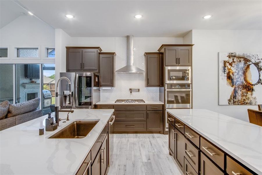 Kitchen with light hardwood / wood-style floors, light stone countertops, wall chimney exhaust hood, appliances with stainless steel finishes, and sink