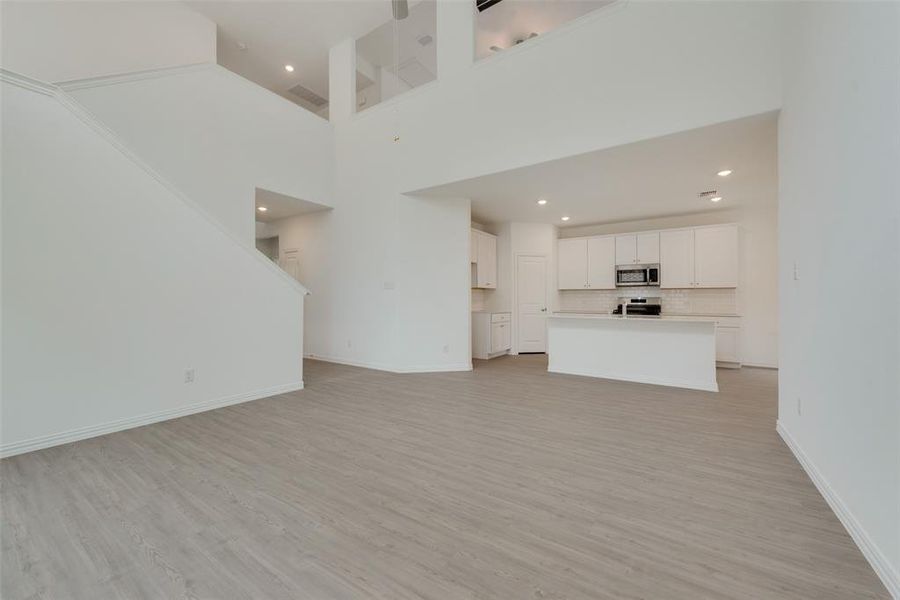 Unfurnished living room featuring a towering ceiling and light hardwood / wood-style floors