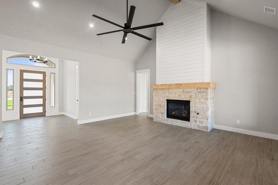 Unfurnished living room featuring hardwood / wood-style flooring, high vaulted ceiling, ceiling fan with notable chandelier, and a stone fireplace