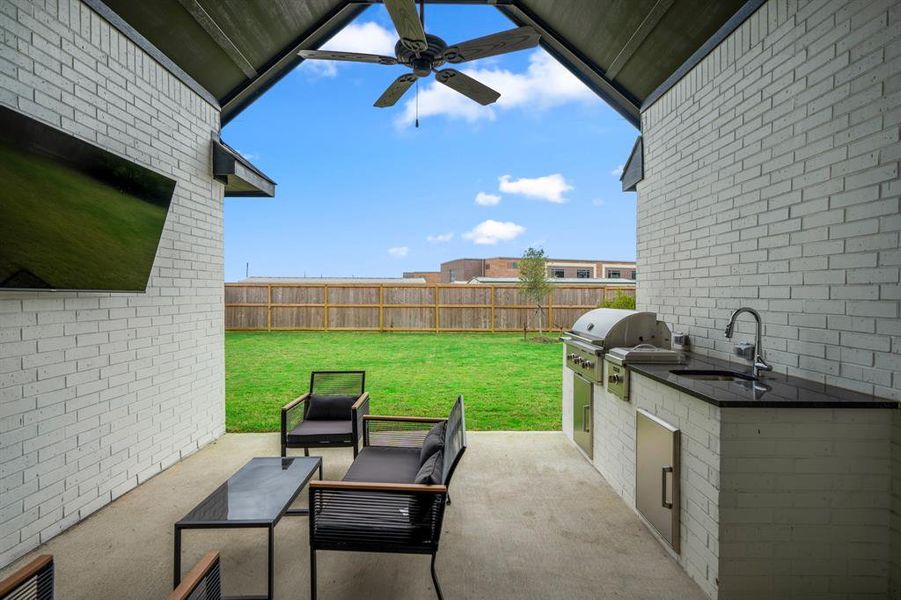 The outdoor kitchen is complete with a built-in stainless still grill, sink, gas burner, and black granite countertops.