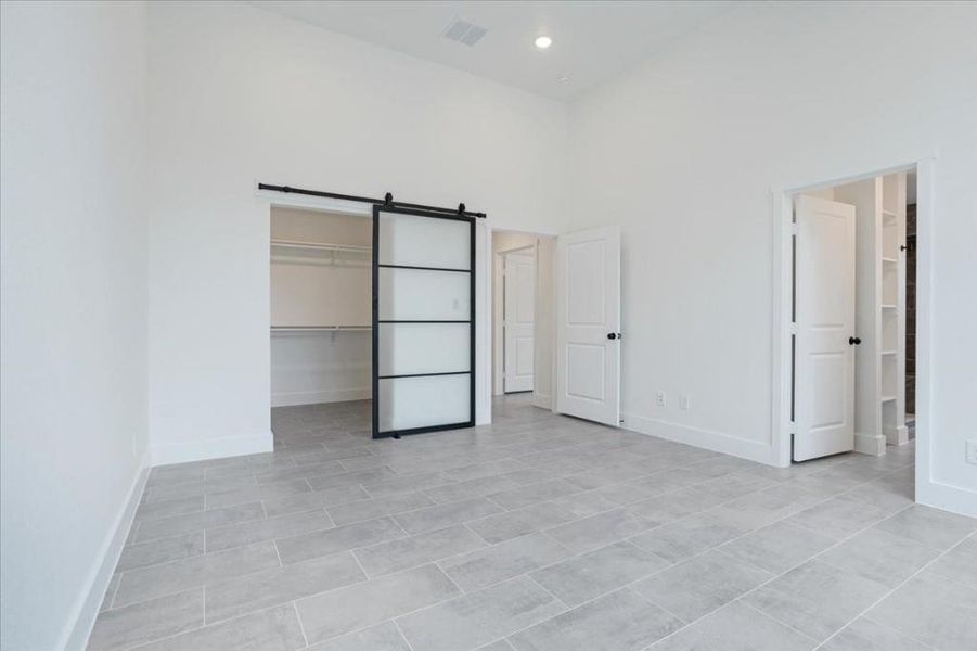 Unfurnished bedroom with light tile patterned floors, a barn door, a towering ceiling, and a closet