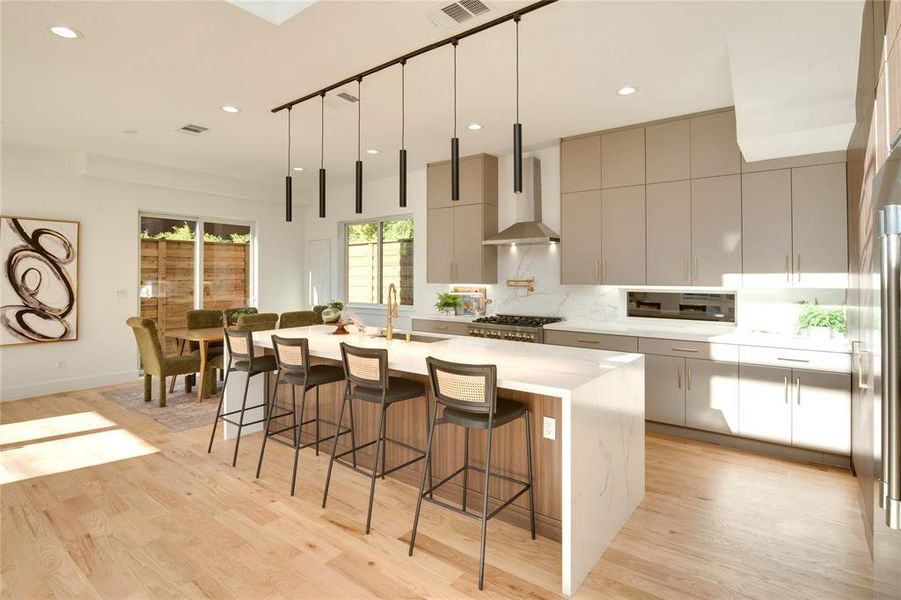 Kitchen featuring light wood-type flooring, hanging light fixtures, a large island, wall chimney exhaust hood, and a breakfast bar