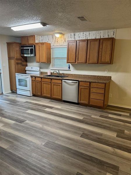 Kitchen with sink, appliances with stainless steel finishes, a textured ceiling, and hardwood / wood-style floors